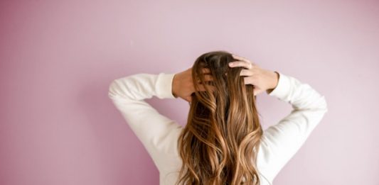 A woman in a white jumper runs her fingers through her hair as we see her from the back.